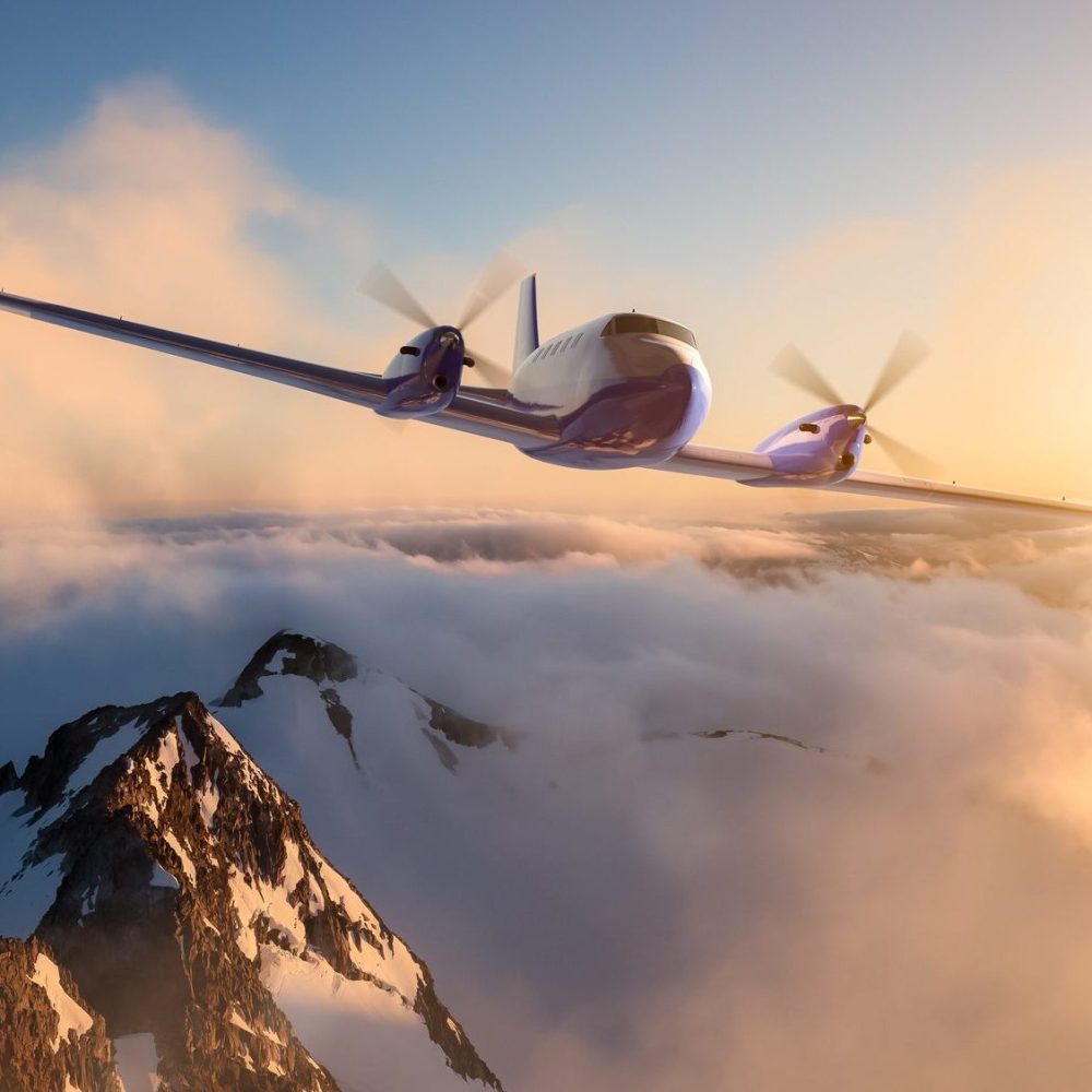 Twin engine airplane flying over Rockies at sunset with clouds below.